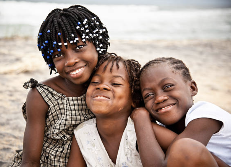 Three smiling Liberian children embracing — representing the AKAA community spirit